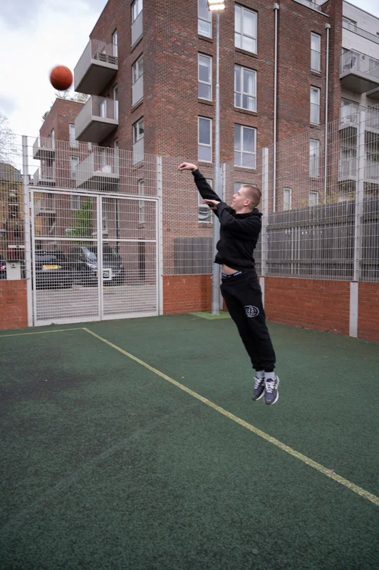 A basketball player rises into a jump shot against the brick buildings.