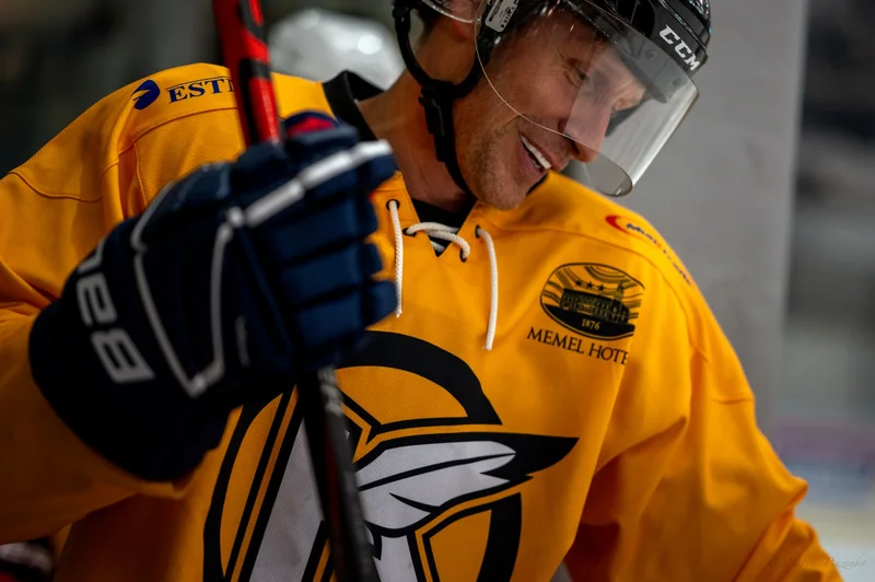 A close smile behind the visor of a yellow-shirted hockey player.
