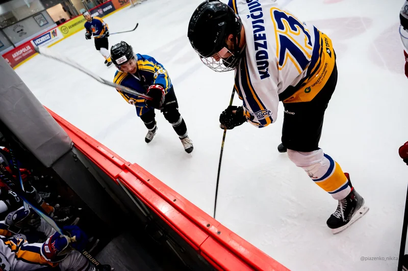 A diagonal, close-range hockey contest over the red rink boundary.