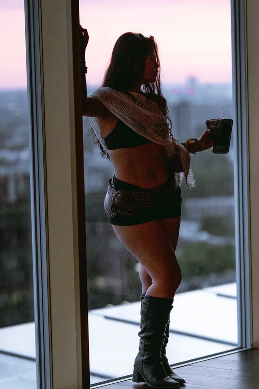 A figure leans into a window frame against the dusk skyline.