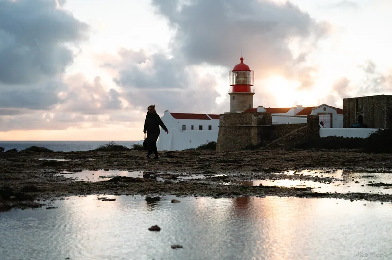 A lighthouse, walking figure and wet rock pool share the last warm light.