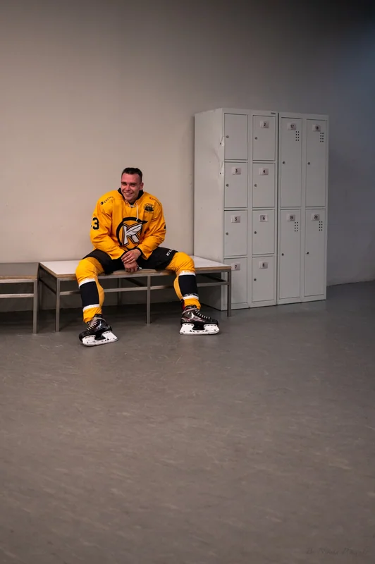 A player smiles alone on the locker-room bench amid quiet grey space.