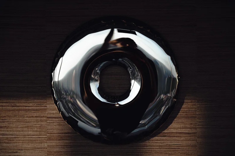A polished circular object catches a clean arc of light against dark wood.