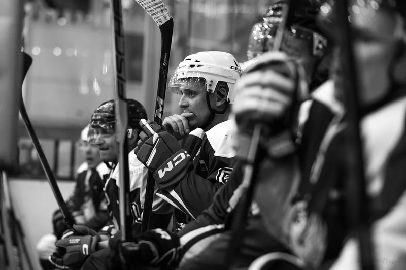 A watchful player on the bench is framed by sticks and teammates.