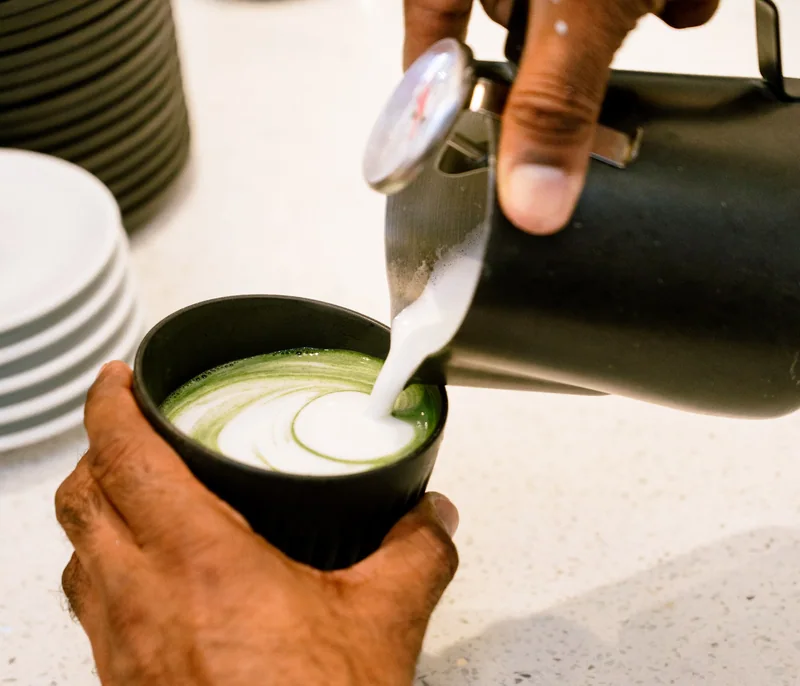 Barista carefully pouring milk into a cup of coffee