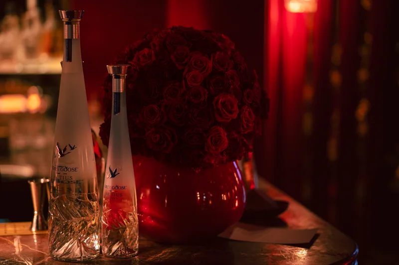 Bottles and glassware beside a red floral display at FashionTV