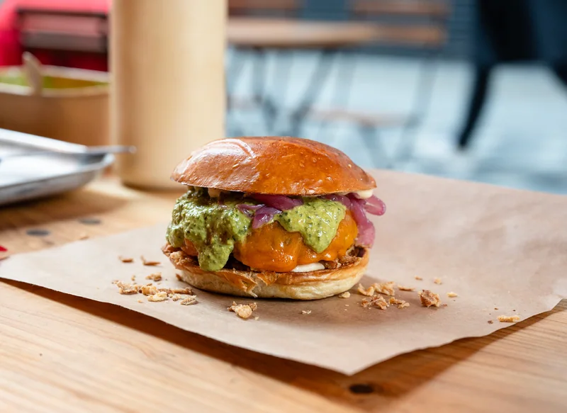 Burger with green sauce on a paper-lined table