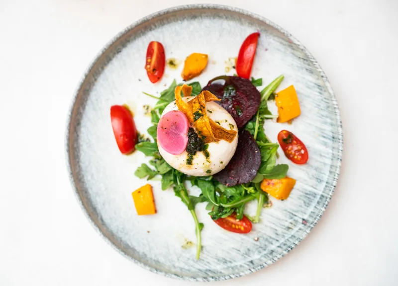 Burrata with tomatoes and colourful vegetables on a pale plate