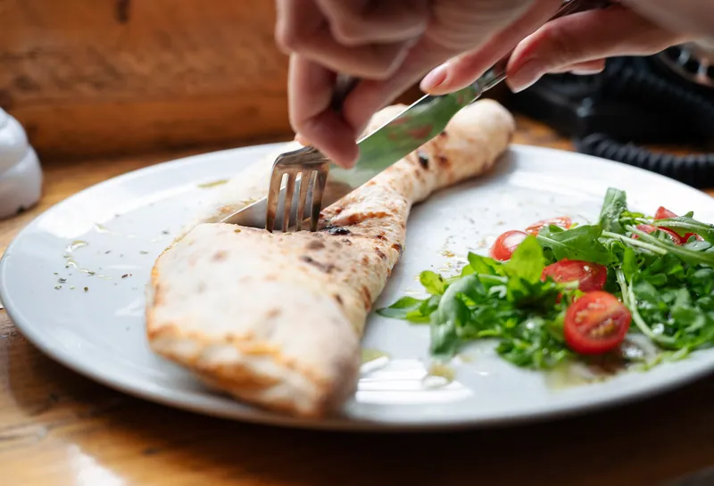 Guest cutting into a calzone beside a salad at Bocca in Cielo