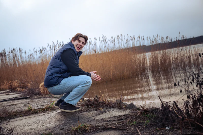 Crouching portrait beside reeds and still water