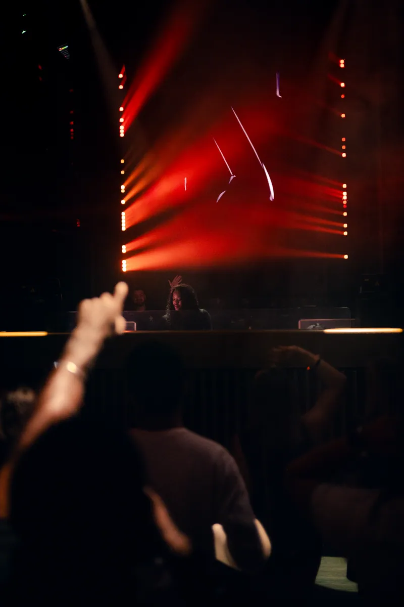 Crowd facing the DJ booth beneath red beams at 77 London