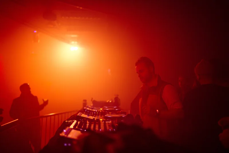 DJ and mixing desk silhouetted in orange haze at E1