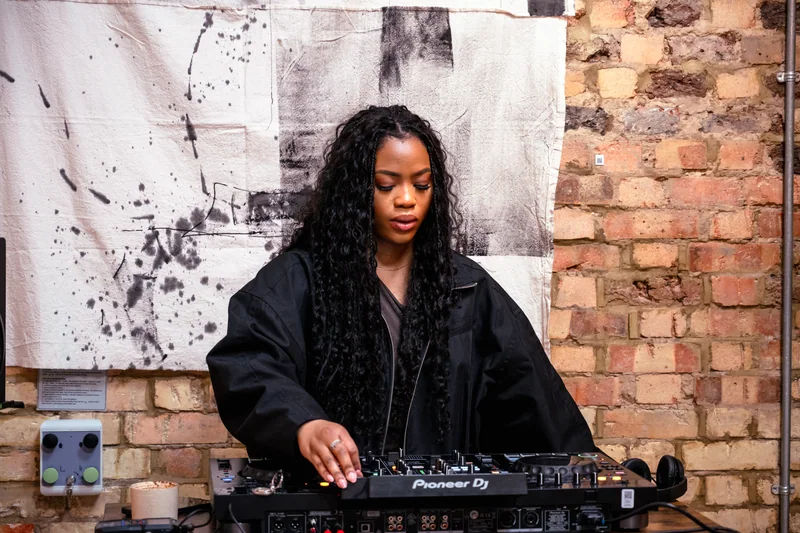 DJ concentrating at the controller against a brick wall at COODIE