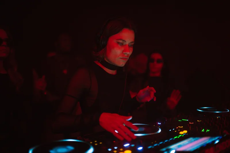 DJ leaning over the mixer under red light at E1