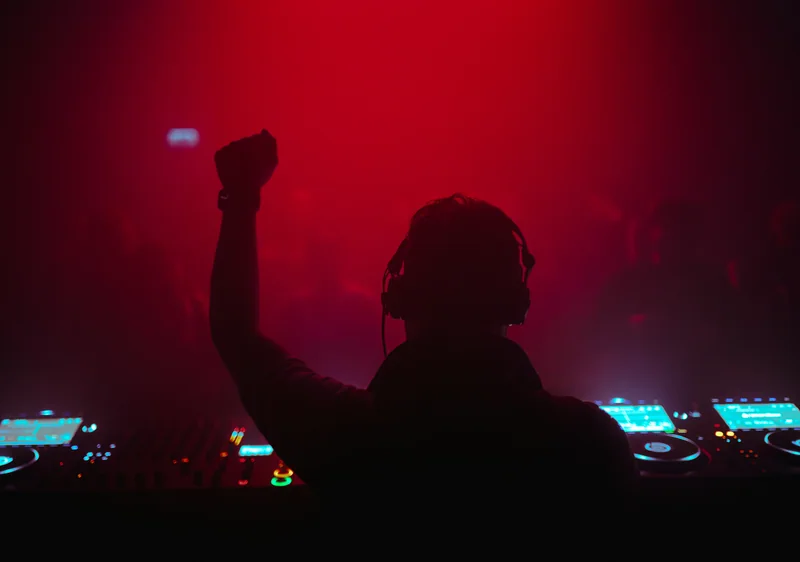 DJ raising a fist towards the crowd in red and violet light