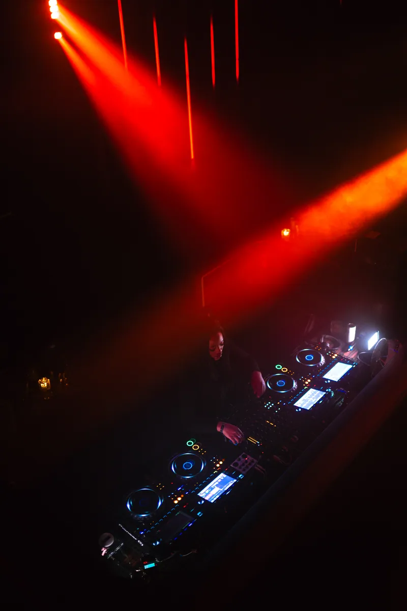 DJ at the decks beneath converging red lights at 77 London