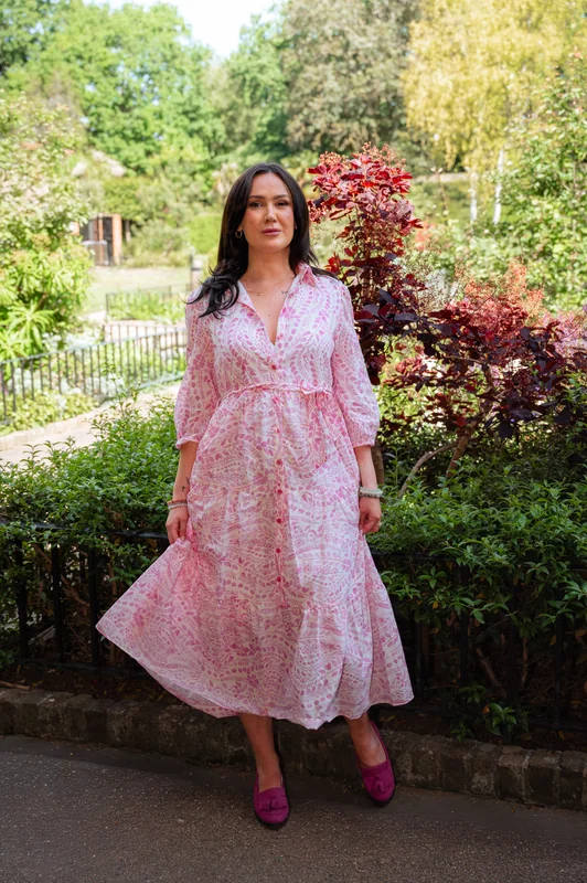 Front-facing full-length portrait in a pink patterned dress in a garden