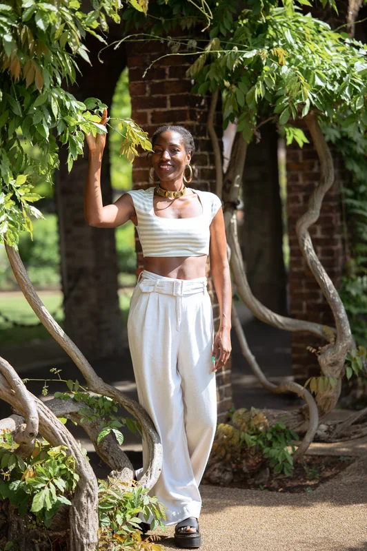 Full-length portrait in a white outfit beneath climbing garden foliage