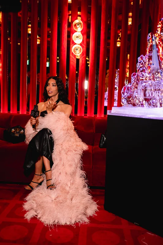 Full-length seated portrait in a pink feathered outfit at FashionTV