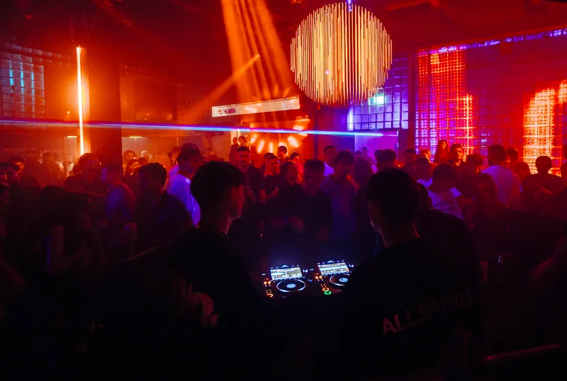 Crowd seen from behind the DJ desk beneath the orange ceiling at Gallery 1986