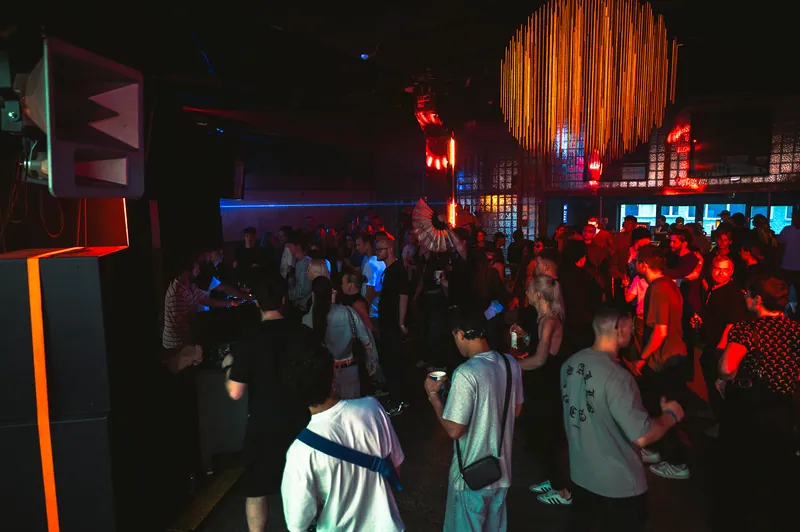 Wide view of the Gallery 1986 room and crowd beneath a glowing ceiling installation