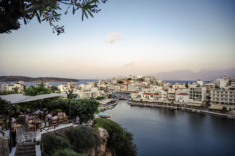 Greek waterfront and hillside café framed by branches at dusk