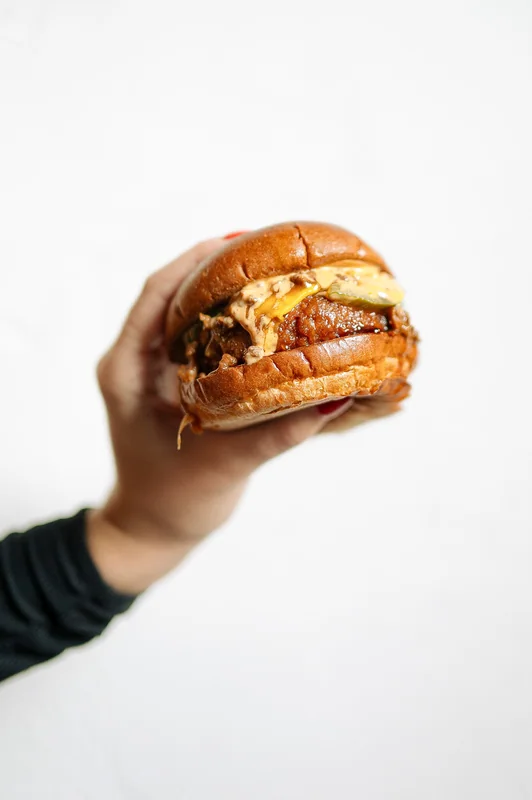 Hand holding a burger against a pale background