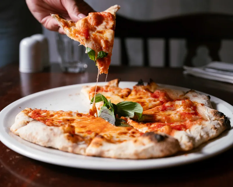 Hand lifting a slice from a freshly served margherita pizza