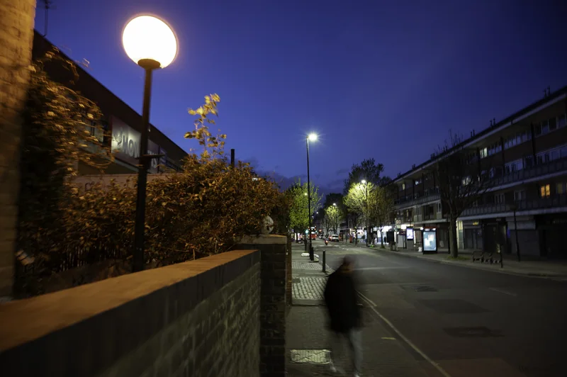 Pedestrian walking beneath round street lamps beside a canal at dusk