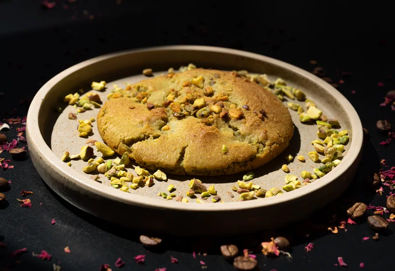 Pistachio cookie on a ceramic plate with nuts and petals against a dark background