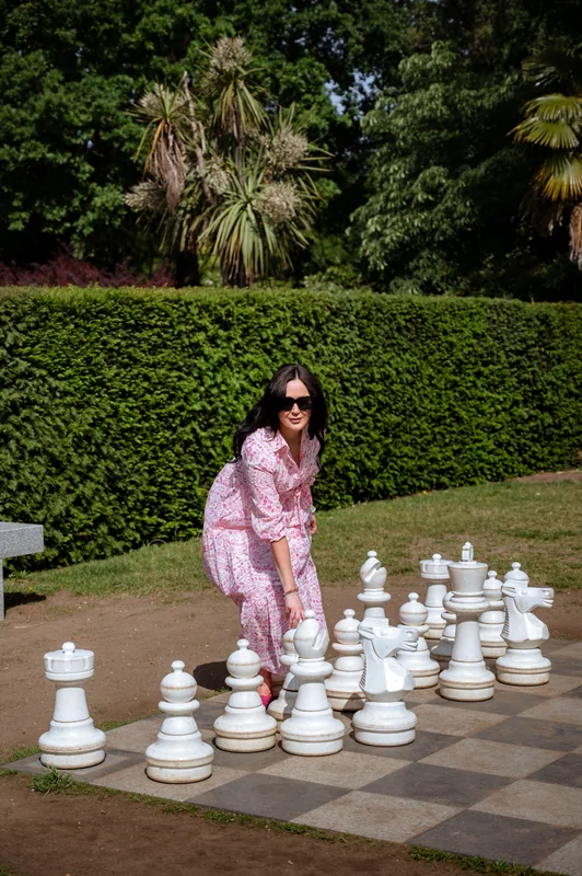 Portrait beside large white chess pieces in a garden