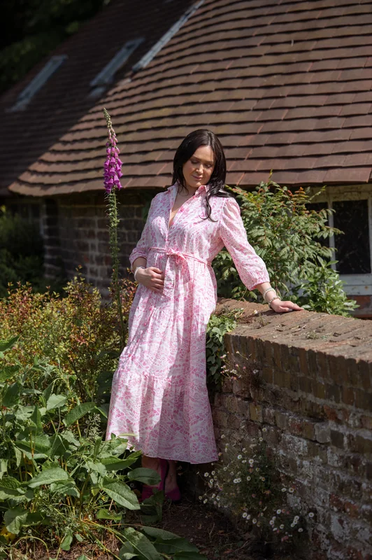 Portrait in a pink dress leaning against a brick garden wall