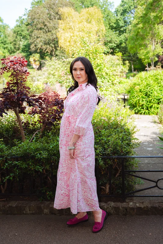 Portrait in a pink patterned dress beside sunlit garden foliage
