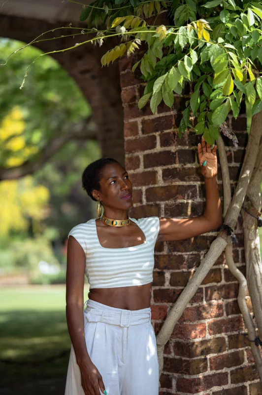 Portrait in a white outfit resting a hand on a shaded brick arch