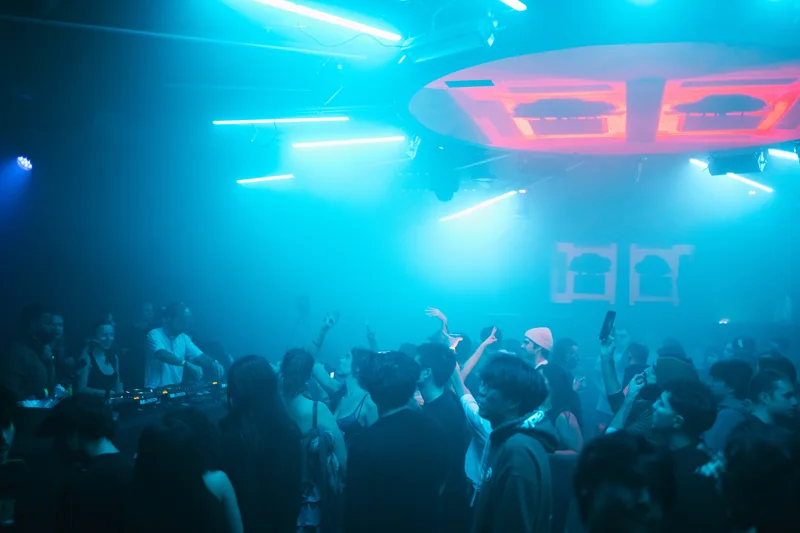 Raised hands in the crowd beneath bright blue lighting at E1