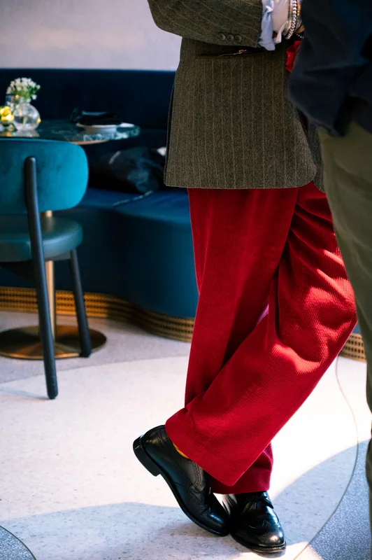 Red trousers and crossed shoes beside blue bar stools