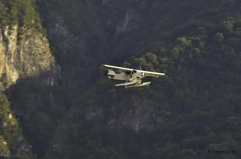 Seaplane flying past a forested mountainside above the lake