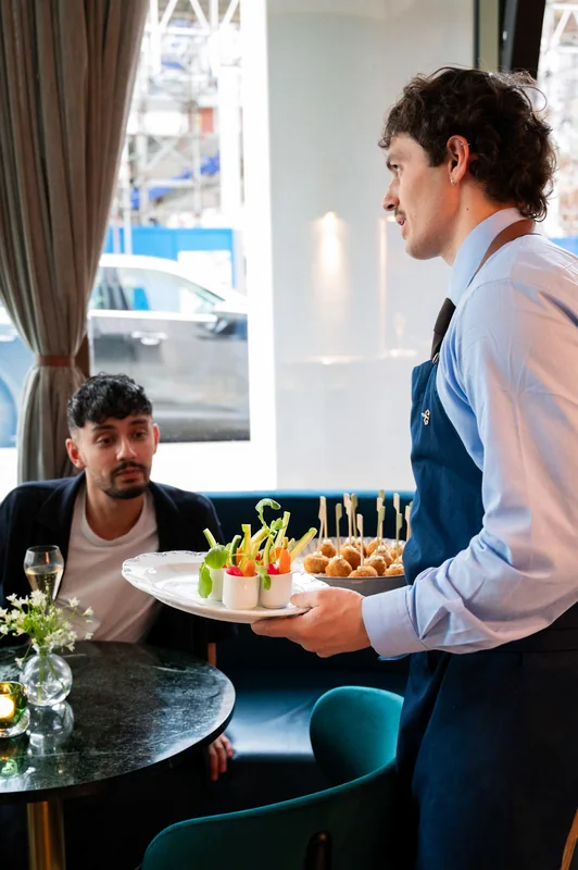 Server presenting food to guests seated by a window at The BoTree