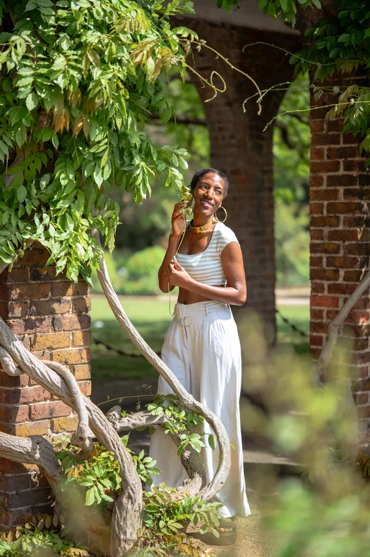 Smiling full-length portrait in white beneath a leafy brick garden arch