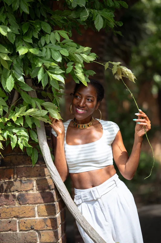 Smiling portrait in a white outfit beside a leafy brick arch