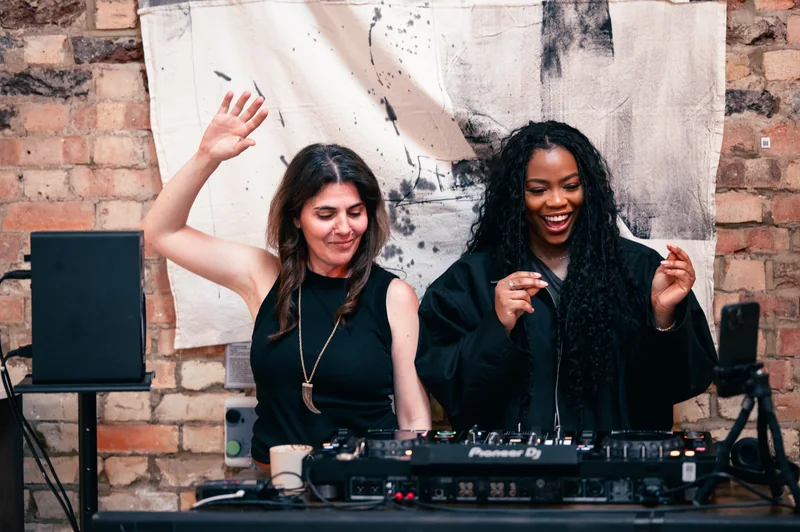 Two guests smiling and dancing beside the COODIE DJ desk