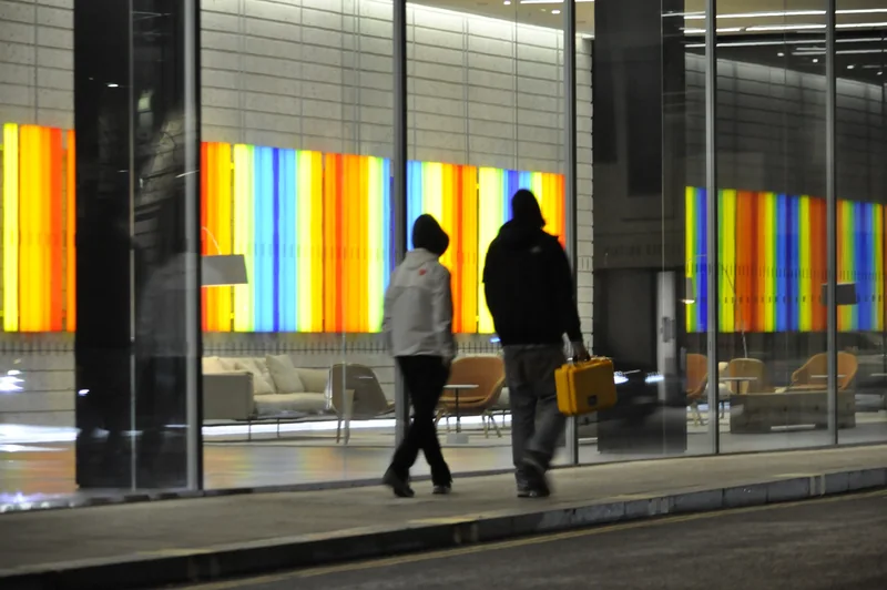 Two people walk past a band of illuminated coloured glass.