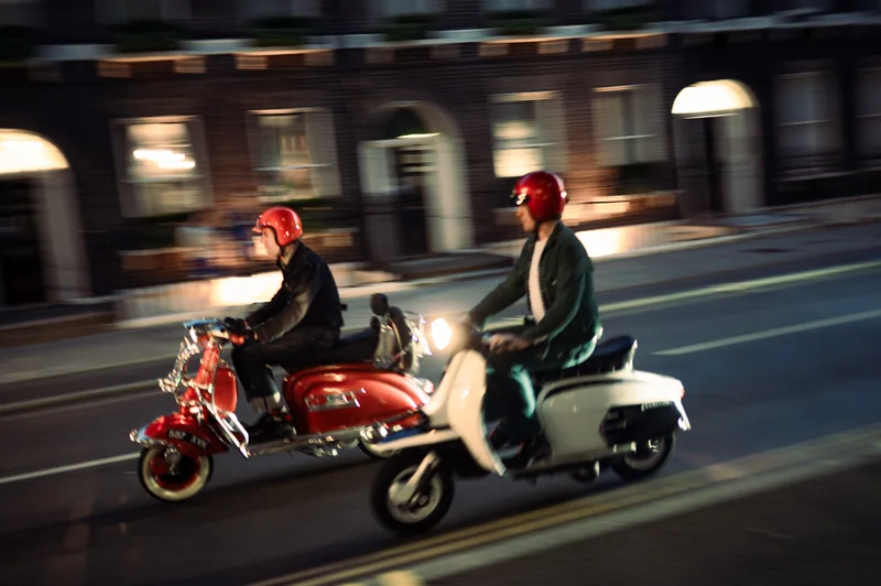 Two scooter riders in red helmets photographed in motion on a London street