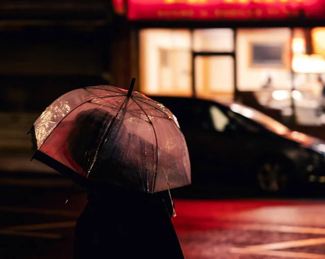 Umbrella and red reflections crossing a London street at night