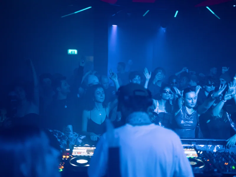 View behind the DJ towards a blue-lit E1 crowd