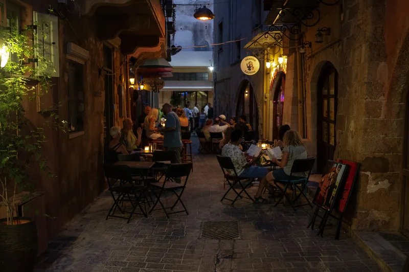 Warm restaurant lights and diners in a narrow Greek lane at evening